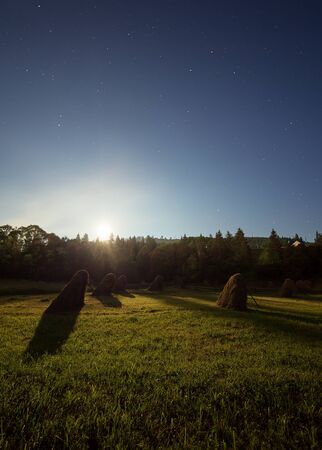Stacks of hay under full moon light with starry sky in carpathian mountains Ukraineの写真素材