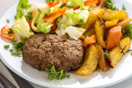 Tasty beef cutlet with salad garnish and potato wedges