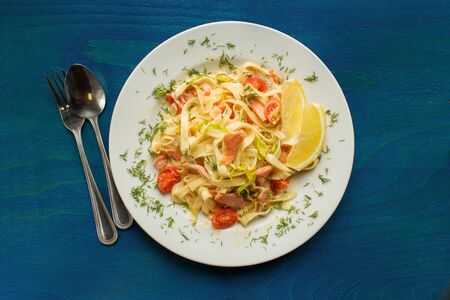 Tasty italian seafood spaghetti with salmon. Tagliatelle pasta with fish, tomato, onion and sauce on blue wooden backgroundの写真素材