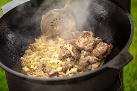 Cooking tasty pilaf in cast iron cauldron. Mutton meat fried with onion in kazan.の写真素材