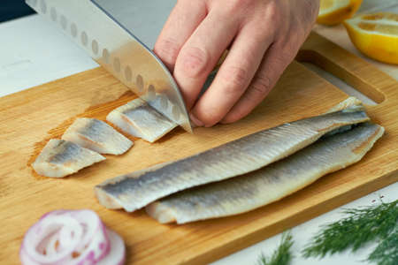 a man is slicing a salted fillet of herring on a cutting board