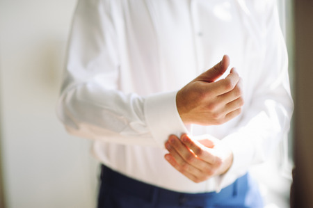 A groom fastening a cuff-link before getting marriedの写真素材