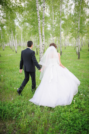 A newly wed couple walking through forrest, holding handsの写真素材