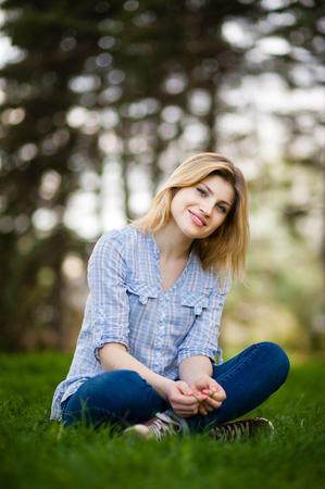 Vertical portrait of a beautiful woman sitting in grass with a smile on her faceの写真素材