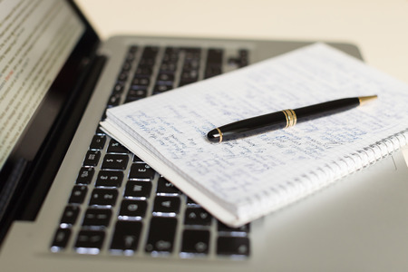 silver laptop computer with notepad, pen on ivory tableの写真素材