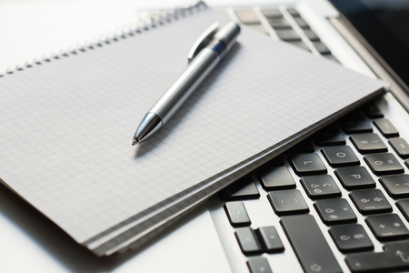 silver laptop computer with notepad, pen on ivory tableの写真素材