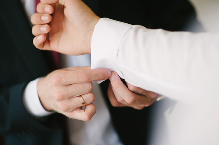 A groom fastening a cuff-link before getting marriedの写真素材