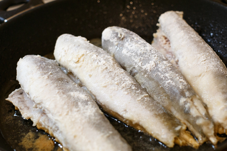 Fried hake fish fillet in a frying pan at kitchenの写真素材