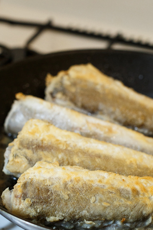 Fried hake fish fillet in a frying pan at kitchenの写真素材