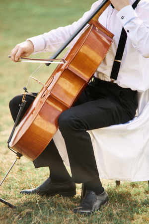 Young man playing cello outside. Cellist playing classical music on celloの写真素材