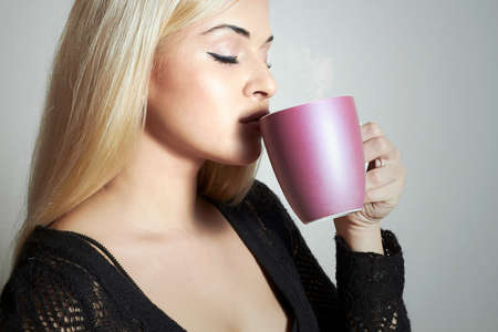 Beautiful woman drinking Coffee. Blond Girl with Cup of tea. Hot drink Deliciousの写真素材