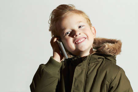funny little boy talking on the cellphone. modern child in winter coat. fashion kids.childrenの写真素材