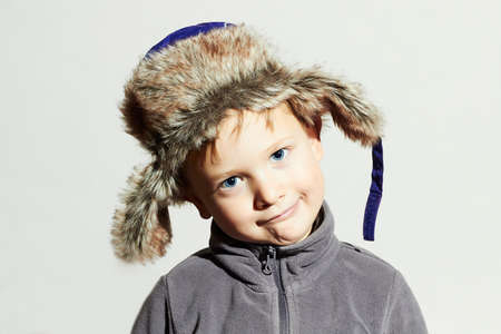 Funny child in fur Hat.casual winter style.close-up portrait of little boy.children emotion.hat ear flaps.Big blue eyesの写真素材