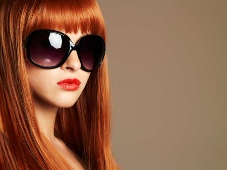 Beauty Girl in sunglasses. Healthy Red Hair. Beautiful Young Woman in sunglasses with red lipsの写真素材