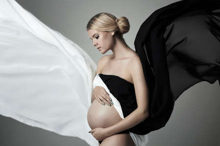 Glamour and style of young beautiful pregnant woman.flying fabric.Blonde girl with big bellyの写真素材