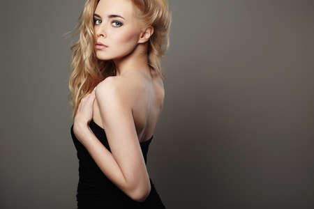 Fashion portrait of beautiful young woman with blond hair. Girl in black dress on grey backgroundの写真素材