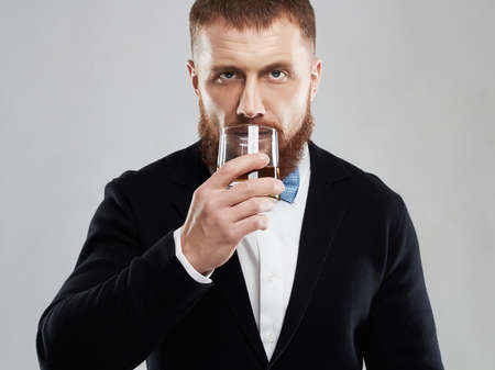 stylish handsome bearded man offers whiskey.Elegant man keeps and holds a glassの写真素材