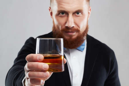 stylish handsome bearded man offers whiskey.Elegant man keeps and holds a glassの写真素材