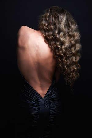 Beautiful back of a young woman in a black dress. Sexy beauty brunette Girl curly healthy hairの写真素材