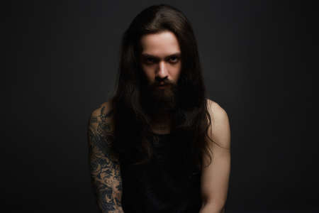 handsome bearded man.Brutal hipster boy with tattoo over dark backgroundの写真素材
