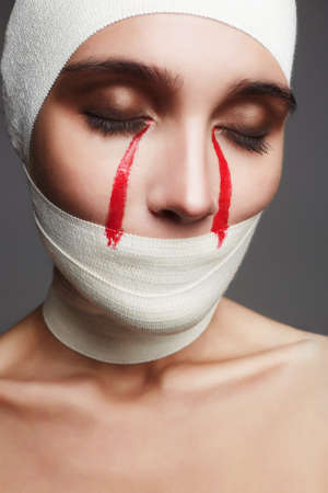 glamorous Halloween card.female face wrapped in bandage.girl with bloody tears.beauty make-up woman.plastic surgeryの写真素材