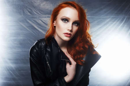 sexy Beautiful young woman portrait in leather coat. red hair girl with make-up looking in camera at studioの写真素材