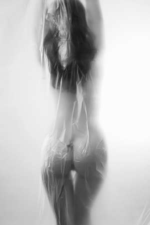 beautiful nude woman silhouette. girl in shower behind a polyethylene film. figure of a naked woman behind a transparent curtainの写真素材
