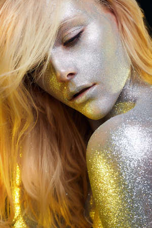 Beautiful Woman with Sparkles. Golden Girl with Art Make-Up in Color Light. Fashion blonde Model with Colorful Makeup and hairの写真素材