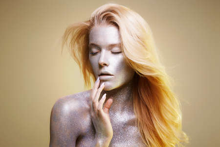 Portrait of Shining Beautiful Woman with Sparkles on her Face and body. Girl with Art Make-Up in Color Light. flying hair Model with Colorful Makeupの写真素材