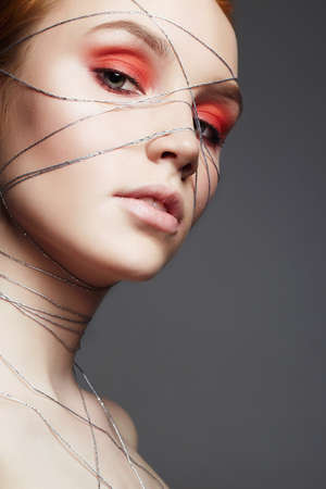 Fashion portrait of beauty make-up girl with orange eye shadow. Beautiful young Woman with makeup and silver thread on the face and Bodyの写真素材