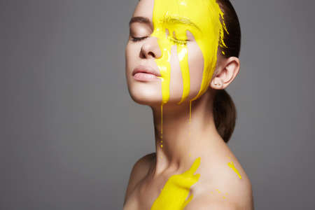 Young woman in Yellow paint. liquid paint flowing over a beautiful face and Body. Color portrait of...