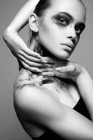 Black and white portrait of Beautiful Young woman with Dirty Paint Face. paint over a face and Body. Girl in Black Paintの写真素材