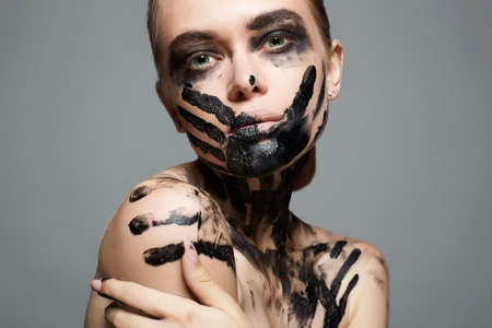 Beautiful Young woman with Paint Face. paint over a face and Body. Halloween style Girl in Black Paintの写真素材