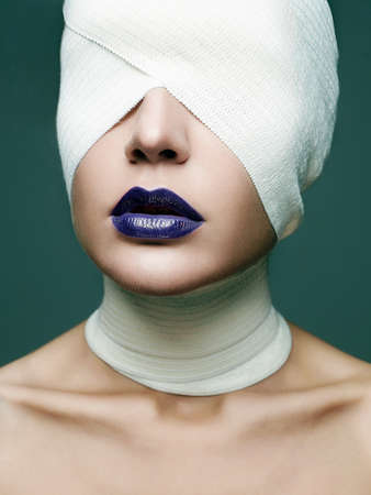 girl in glamorous mask for halloween. female face wrapped in bandage. beauty make-up woman, blue lipstick. plastic surgeryの写真素材