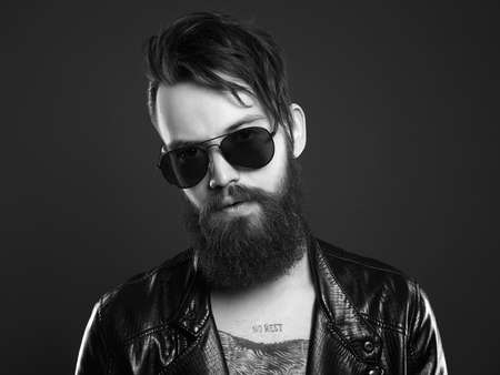 fashionable handsome man in sunglasses. Hipster bearded boy in leather coat and trendy glasses. black and white portraitの写真素材