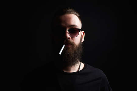 Hipster boy with cigarette. handsome Brutal bearded smoking man in sunglassesの写真素材