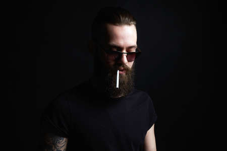 Hipster boy with cigarette. handsome Brutal bearded smoking man in sunglassesの写真素材