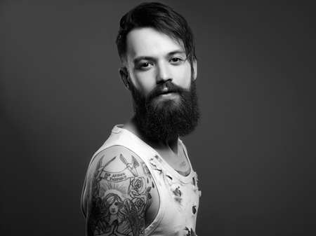 black and white portrait of handsome man with beard and tattoo. bearded hipster boy in vintage torn dirty shirtの写真素材