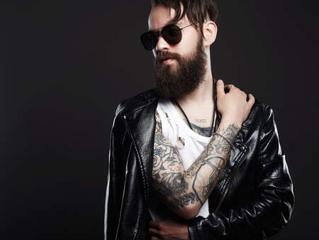 fashionable tattooed handsome man in sunglasses. Brutal bearded Sexy boy in leather coatの写真素材