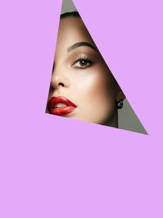 Beautiful red lips young woman into the hole of purple paper. Beautyportrait of  girl with make-up.の写真素材