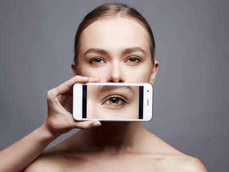 Beautiful girl with a phone instead of a mouth. social networks. eye on screen. social photo. woman in internetの写真素材