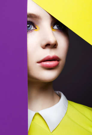 Beautiful young woman into the hole of color paper. Beauty portrait of girl with colorful make-upの写真素材