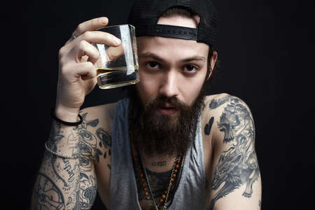 handsome bearded man with tattoo enjoying whiskey. tattooed man in hat drinking a whiskeyの写真素材