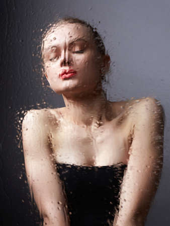 beautiful  girl behind wet glass. sensual young woman in bathroomの写真素材