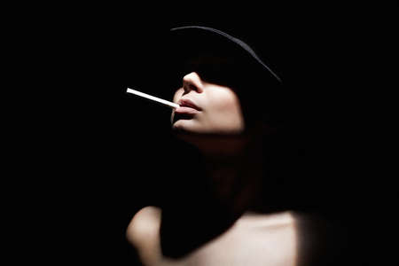 Beautiful woman in a hat and with a cigarette. Retro style portrait. Girs face under Shadow