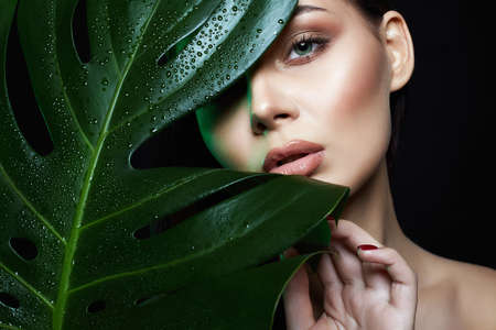 beautiful girl in palm leaves. Beautiful young woman with Make-up. Beauty Portrait. Natural...