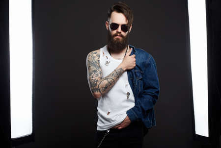 Tattooed handsome Bearded Man in sunglasses and Denim. Brutal hipster boy with tattoo. Male model in Photostudioの写真素材