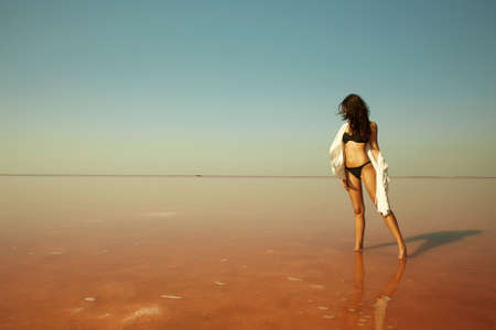 beautiful girl standing in the water on a pink salt lake. relaxing young woman in bikiniの写真素材