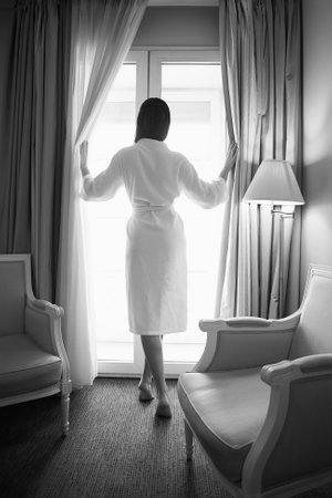 Woman in bathrobe stay near the window in hotel room. Female back. Black and white photoの写真素材