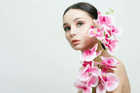Beautiful young Woman with Flowers. Beauty Portrait of Girl with Orchid flower. Clean Skin Face, careの写真素材